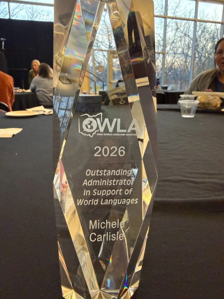A crystal trophy engraved with the Ohio World Language Association logo, the year 2026, "Outstanding Administrator in Support of World Languages," and the name Michele Carlisle.