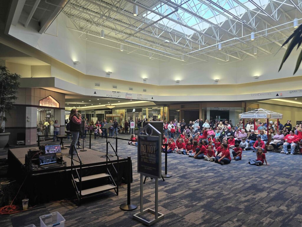 A student performs on stage at the Ohio Valley Mall while a large crowd, including rows of students in red shirts, watches the live performance during the Celebration of the Arts.
