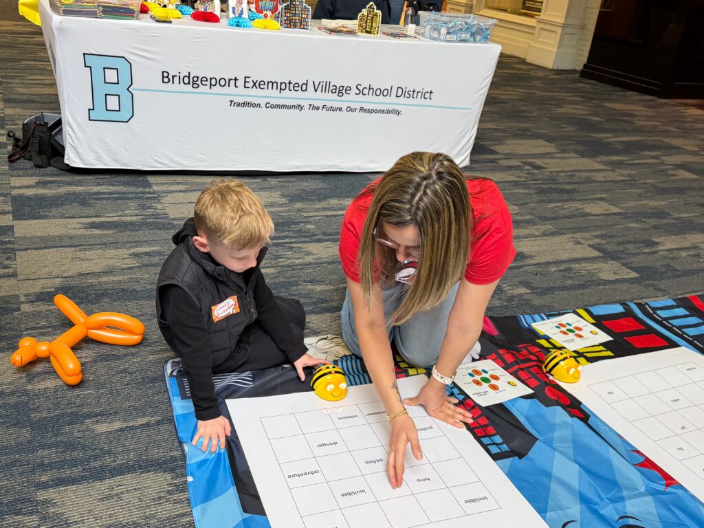A teacher points to a large activity sheet on a table while a child looks on at the Bridgeport Exempted Village School District booth.