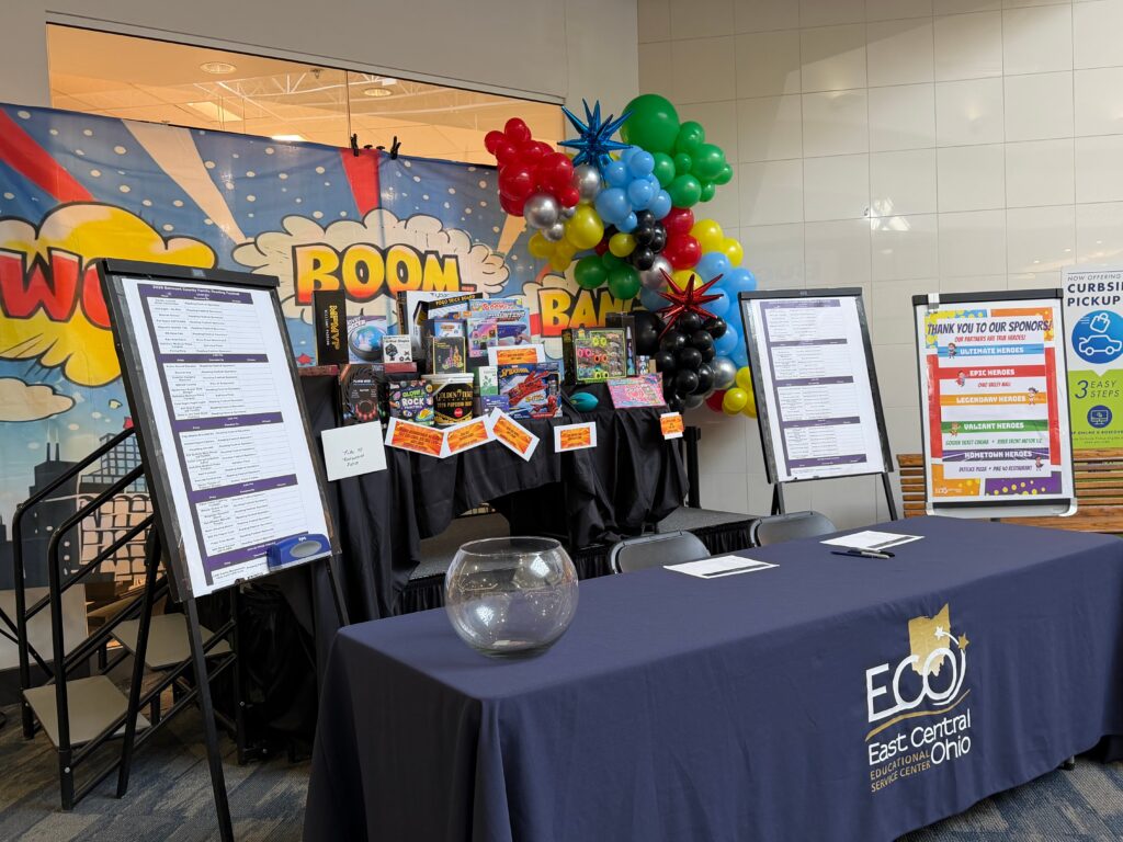 A decorated ECOESC booth featuring superhero-themed balloons, displays, and signage in a mall setting.