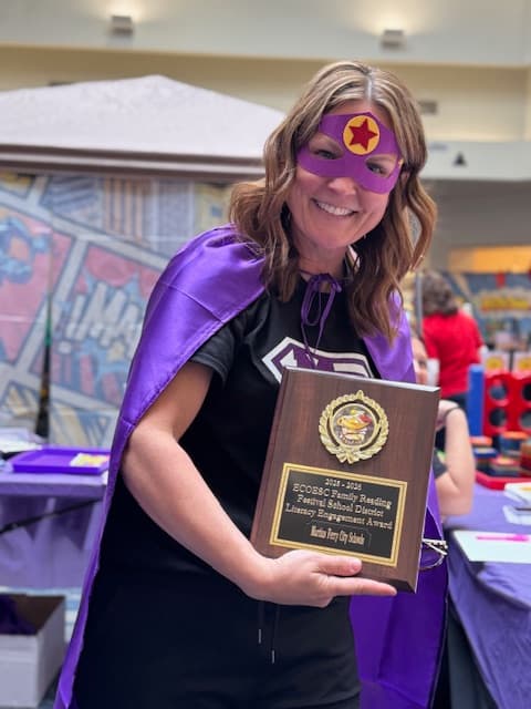 A woman dressed in a purple superhero cape and mask smiles while holding an award plaque at the festival.